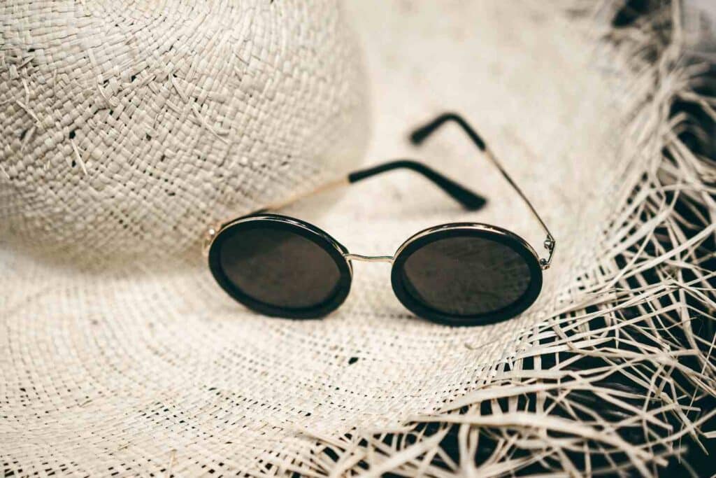 A stylish pair of summer sunglasses resting next to a wide-brim sun hat under bright sunlight.