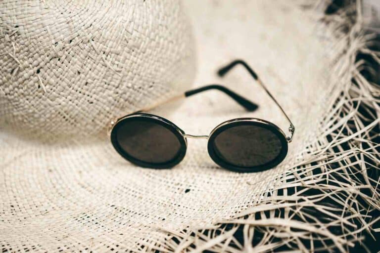 A stylish pair of summer sunglasses resting next to a wide-brim sun hat under bright sunlight.